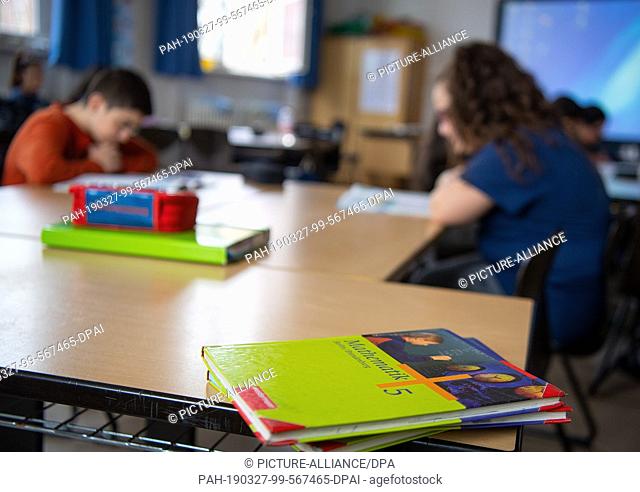 27 March 2019, Berlin: Textbooks lie on a table in a classroom of a primary school, while pupils take part in lessons in the background