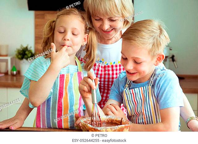 Happy grandmother with her grandchildren having fun during baking muffins and cookies