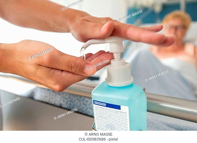 Nurse using hand sanitiser on hospital bed