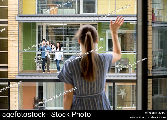 Back view of woman standing on balcony waving to her neighbours