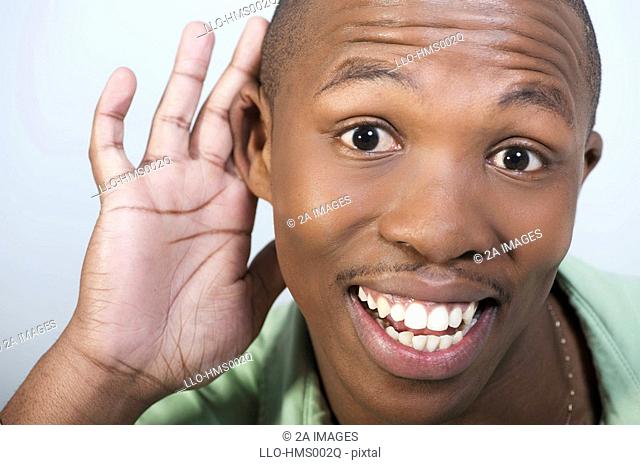 Close-up of a young man with his hand to his ear trying to listen, against a white background, Johannesburg, Gauteng Province, South Africa