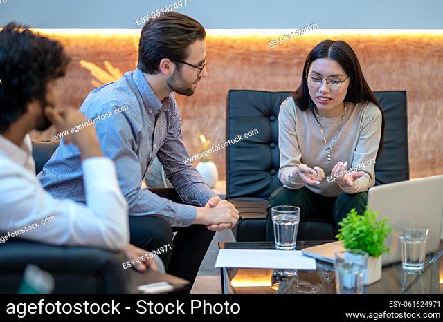 Company employee seated at the coffee table next to her male colleagues pointing at the laptop