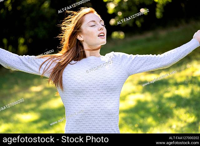 Young woman with eyes closed stretching her arms in park