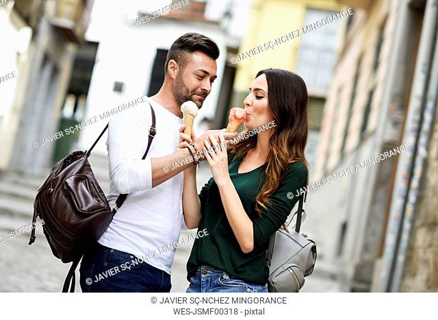 Tourist couple sharing ice cream cones in the city