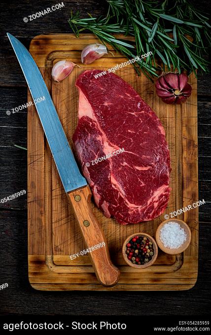 Raw ribeye beef steak with herbs and spices from above on wooden rustic table