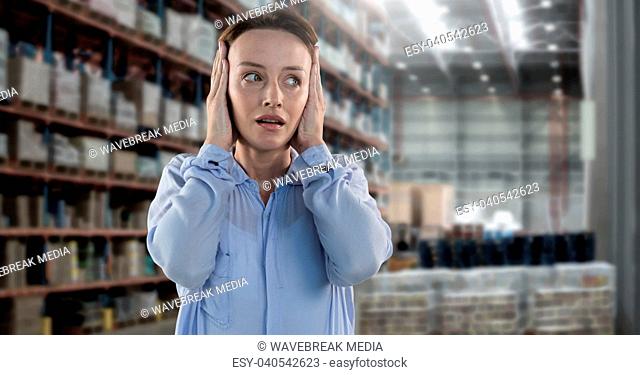 Businesswoman in warehouse covering ears and worried