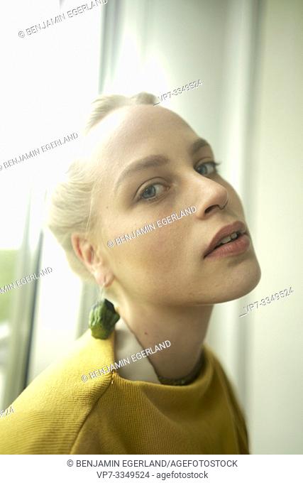 young woman wearing earring made of raw zucchini, chin raised