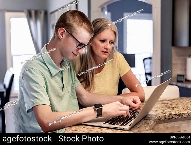 Young man uses a laptop computer at home with support from his mother; Edmonton, Alberta, Canada