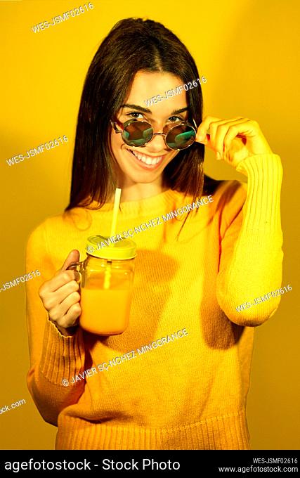 Happy woman holding glass of orange juice against yellow background