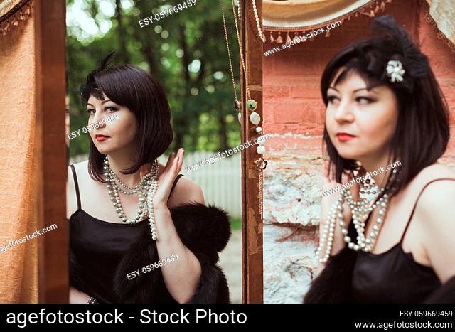 Portrait of a woman in retro style, looking in the mirror and holding a necklace