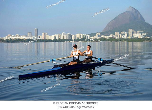 Two young women participating in early morning rowing training in the Lagoa Rodrigo de Freitas Lagoon, with Rio de Janeiro skyline and Sugar Loaf Mountain