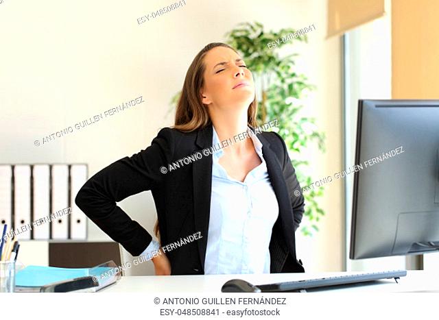 Unhappy businesswoman suffering back ache sitting on an uncomfortable seat at work indoors in her office