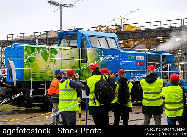 24 November 2022, Saxony-Anhalt, Stendal: Media representatives and Alstom employees stand in front of a hydrogen-powered shunting locomotive from which steam...