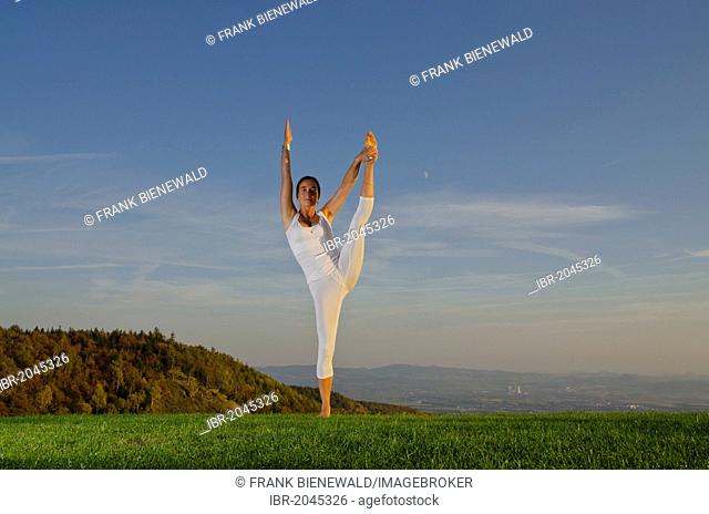 Young woman practising Hatha yoga outdoors, showing the pose anjaneyasana, raised hand to foot pose, Nove Mesto, Okres Teplice, Czech Republik, Europe