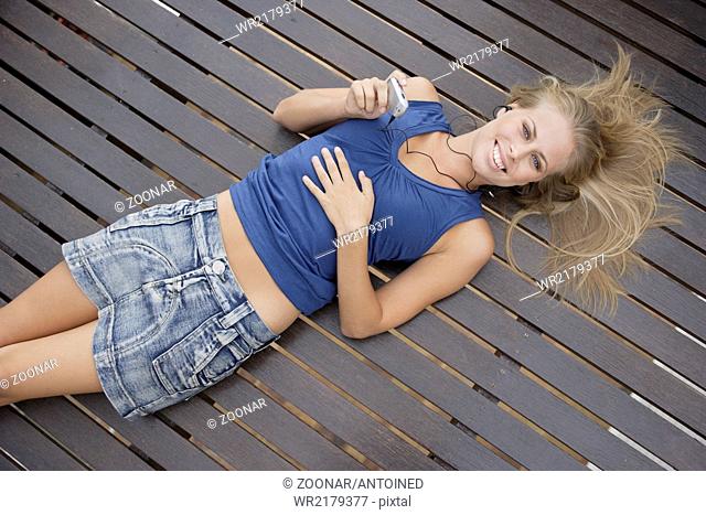 Young woman with MP3 player lying on woodenfloor