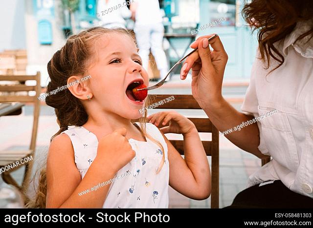 Young long-haired mom eating cake with smiling kid on the street