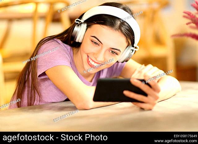 Happy female watching videos on smart phone wearing headphones at home