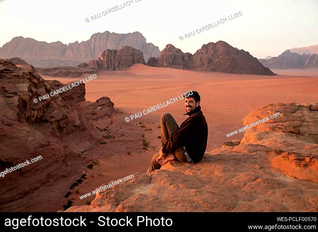 Happy young man sitting on rock in the desert at sunset