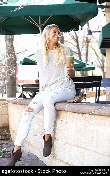 Woman at a cafe holding iced coffee looking back over her shoulder laughing