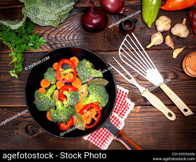 fresh vegetables in a black round frying pan on a brown wooden background, top view