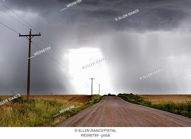 Rural thunderstorm scene showing dirt road leading to a bright light opening up between looming cumulus thunder clouds releasing rain