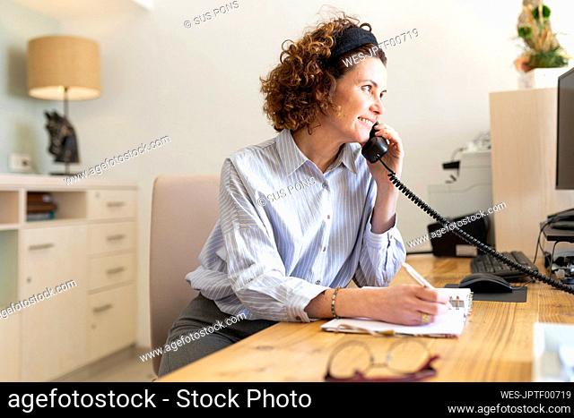 Female receptionist writing in dairy while talking on telephone at hotel