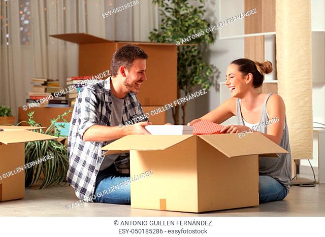 Happy couple laughing unboxing belongings moving house sitting on the floor in the night