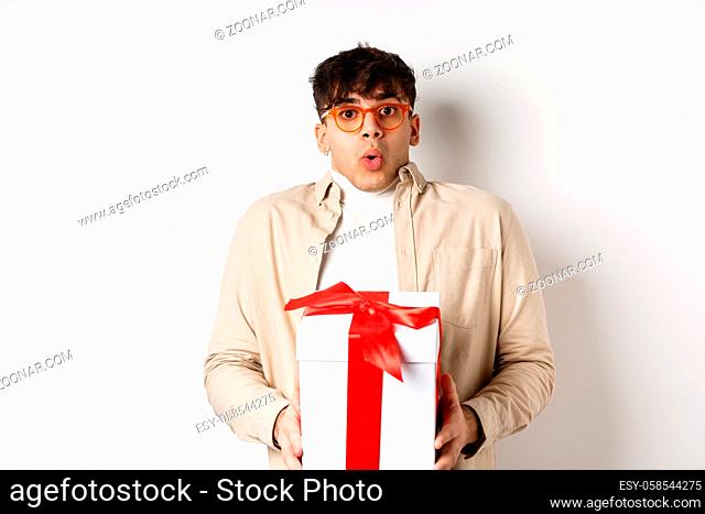 Surprised young man say wow and holding gift box, receive present on holiday, standing amused on white background