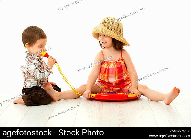 Happy kids playing on toy music instrument, little boy singing to microphone over white background