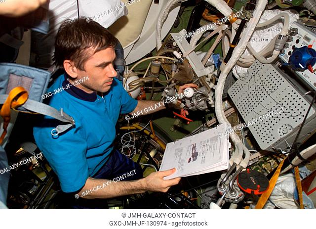 Cosmonaut Yuri I. Malenchenko, Expedition 7 mission commander representing Rosaviakosmos, looks over procedures checklists in a Soyuz spacecraft docked to the...