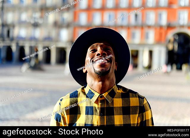 Smiling african man wearing hat looking up while standing in city
