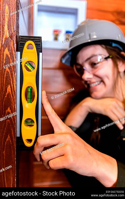 selective focus of spirit level on woman's hand, she wore a grey hard hat as she smiling in the background during a home inspection. vertical