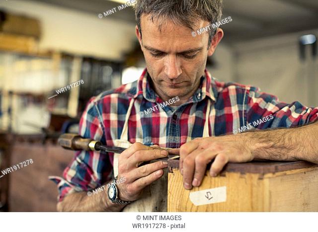 An antique furniture restorer working with his hands using a sharp tool on the edge of a piece of wooden furniture