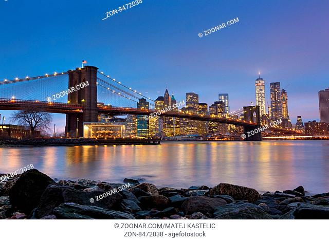 Brooklyn bridge and New York City Manhattan downtown skyline at dusk with skyscrapers illuminated over East River panorama