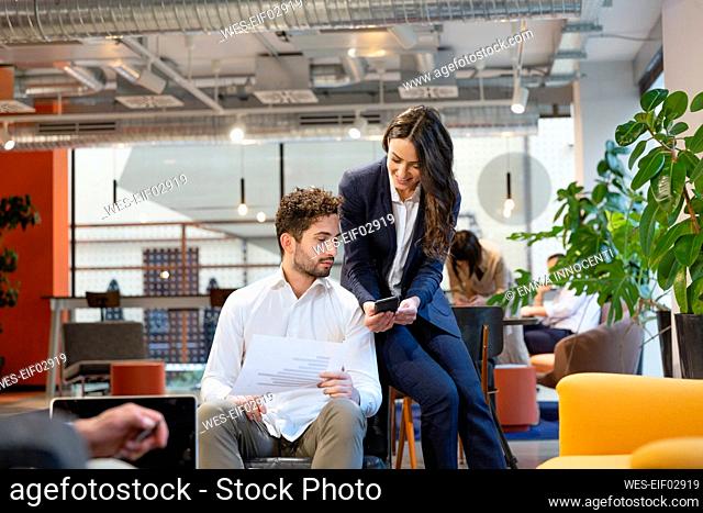 Businesswoman sharing smart phone with colleague in office