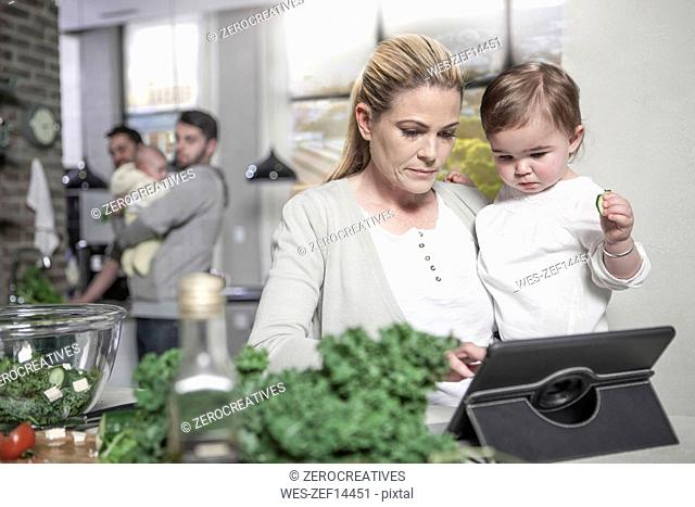 Mother holding baby using tablet in kitchen