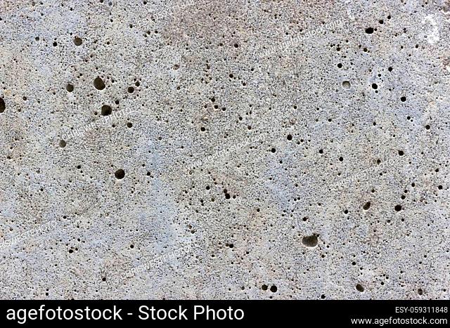 A flat grey concrete surface. The surface is textured and covered in holes from lots of tiny air bubbles
