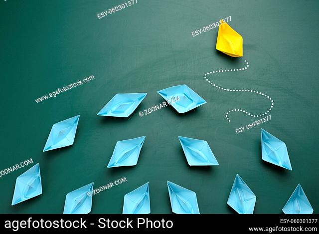 group of blue paper boats are sailing in one direction, one yellow is sailing in the opposite direction. The concept of an extraordinary personality
