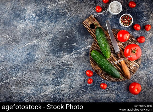 The concept of healthy eating with organic cucumber and set of tomatoes on wooden cutting board. Top view. Space for text