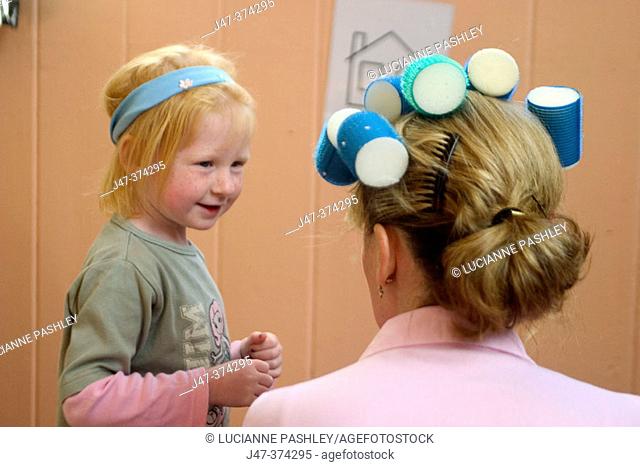 Little girl pretending to be a hairdresser, putting rollers in teachers hair