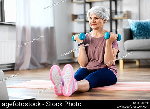 woman with laptop and dumbbells exercising at home