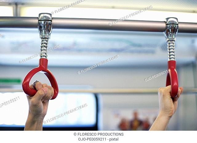 Two hands holding bus handles