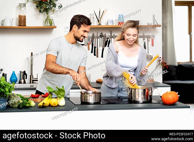 Smiling young man looking at girlfriend making pasta in kitchen