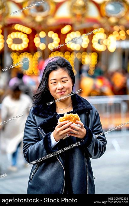 Smiling young woman holding burger at amusement park