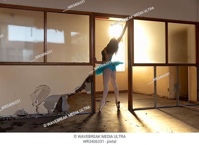 Rear view of a young mixed race female ballet dancer wearing a blue tutu and pointe shoes dancing in a doorway at an abandoned warehouse building