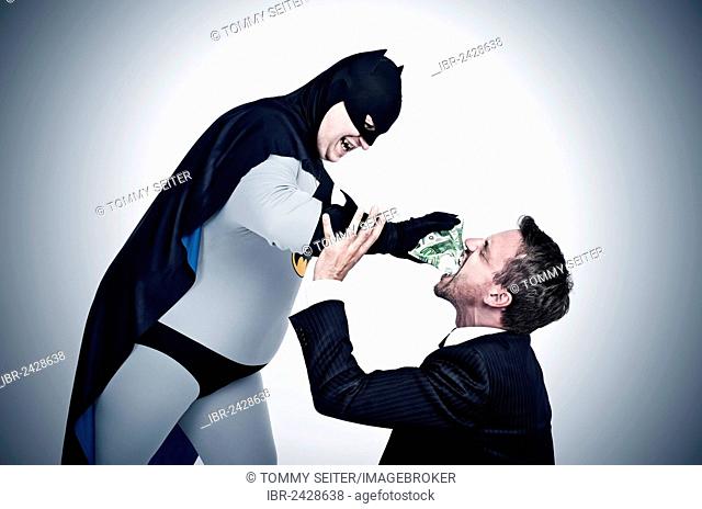 Chubby superhero wearing a Batman costume stuffing money into the mouth of a man wearing a suit