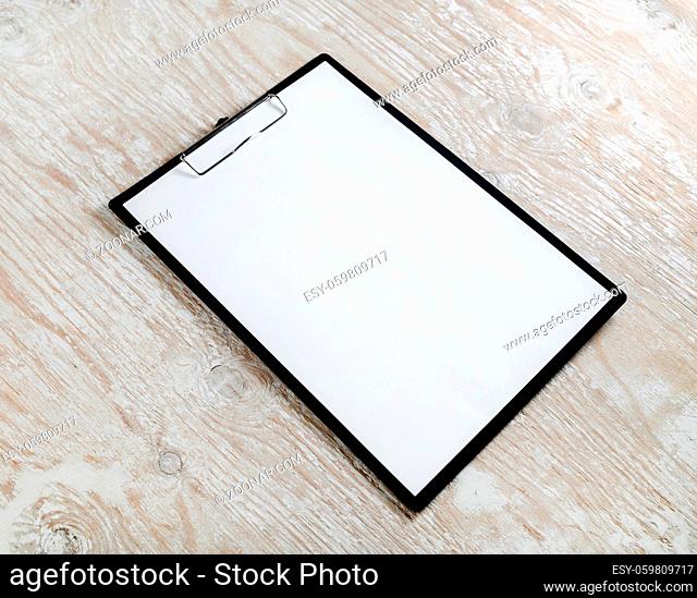 Photo of clipboard with a blank sheet of paper on light wooden background with plenty of copy space. Blank template for design presentations and portfolios