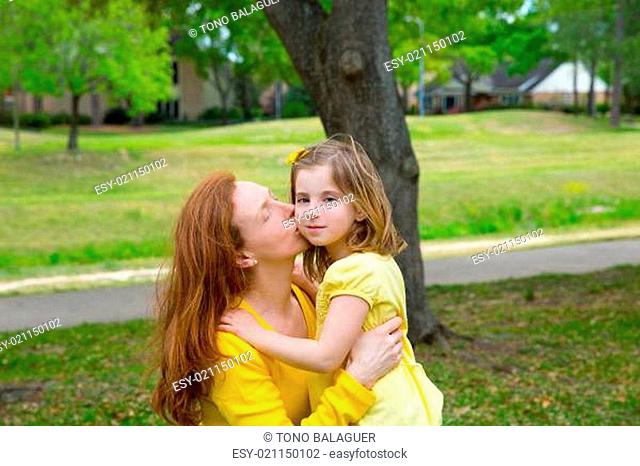Mother kissing her blond daughter in green park