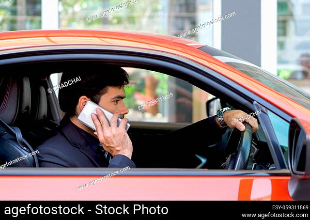 Young businessman in a black suit using mobile phone while holding the car wheel