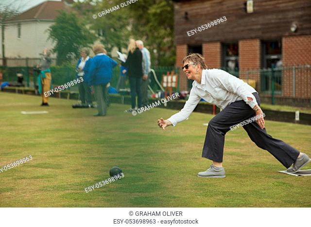 A side view shot of a happy senior woman taking her shot in a game of lawn bowling